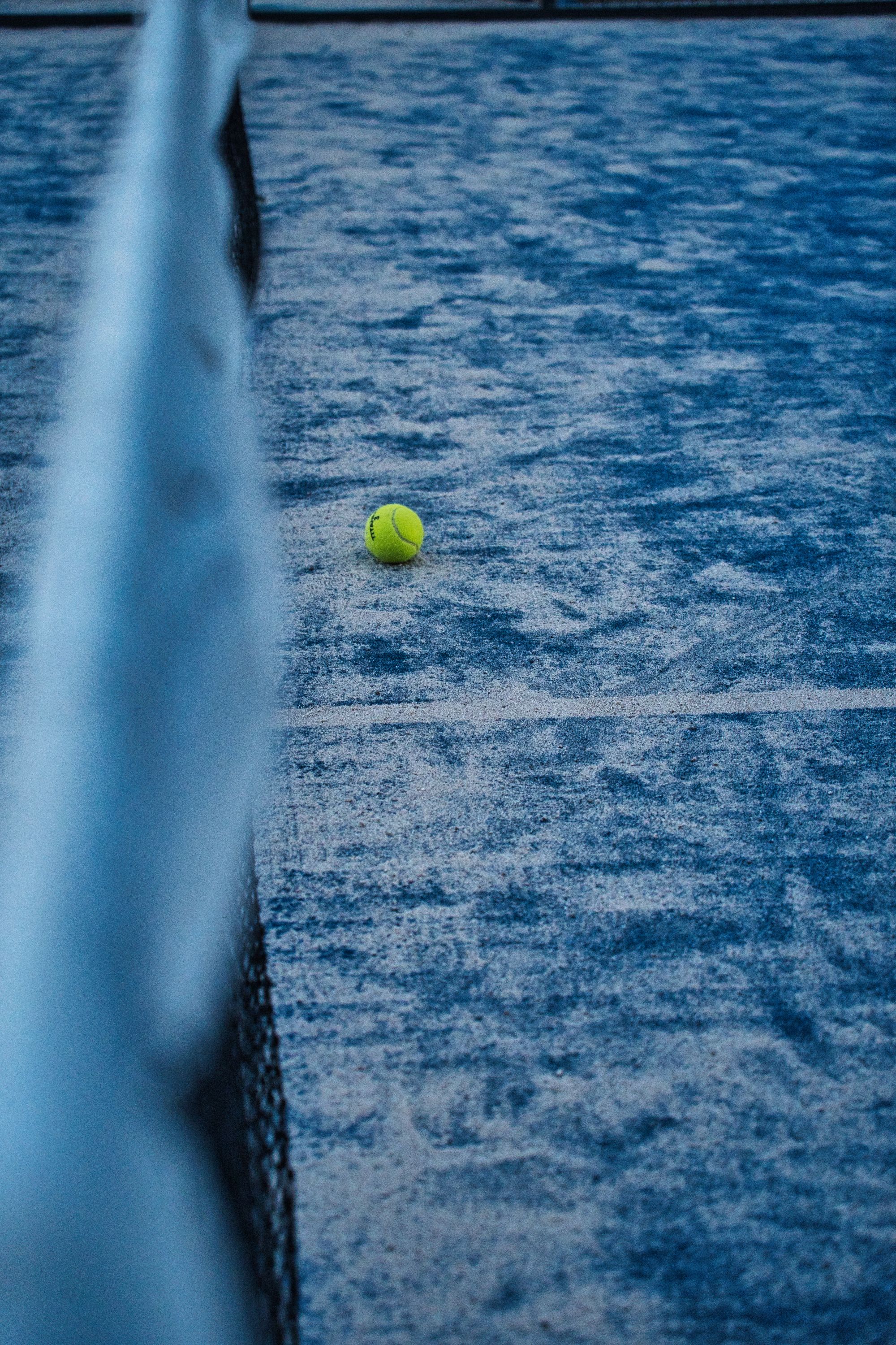 Padel ball resting on a blue court beside the net